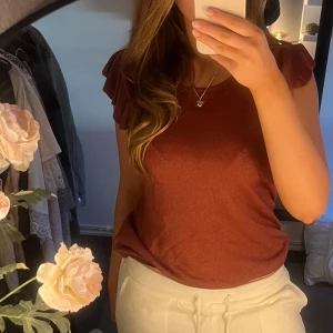 Rostfärgad topp - Säljer en snygg  topp med korta volang ärmar. Perfekt för både vardag och lite finare tillfällen. Toppen har en enkel och stilren design som gör den lätt att matcha med olika outfits. Perfekt till sommaren! Jättefint sick och knappt använd❤️passar M-S storleksmässigt 