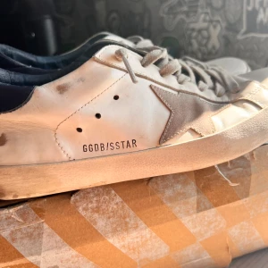 Vita golden goose - Snygga vita sneakers från Golden Goose med en ikonisk stjärndetalj i silver på sidan. Skorna har en rund tå och snörning framtill. Perfekta för en avslappnad stil med en touch av lyx. De har blivit limmade i fram. Hör av dig vid minsta fundering!