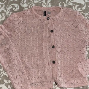skofta från H&M - Säljer en söt rosa spetskofta från H&M med dekorativa knappar framtill. Koftan har ett fint spetsmönster och långa ärmar, perfekt för att lägga till en romantisk touch till din outfit. 💖