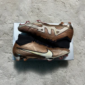 Nike mercurial superfly 15  - Snygga bronsfärgade fotbollsskor från Nike med svart snörning och vit swoosh-logga. Skorna har en strömlinjeformad design med mönstrade detaljer och en robust sula för optimalt grepp på planen. (Skick: 8/10)