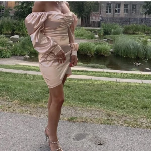 Ljusrosa  offshoulder klänning - Elegant rosa klänning med offshoulder-design Klänningen har en åtsittande passform och är tillverkad i ett glansigt material som ger en lyxig känsla. Perfekt för speciella tillfällen.