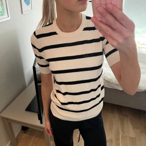 Randig tröja från Zara - Säljer en stilren randig tröja från Zara i beige och svart. Tröjan har korta ärmar och en rund halsringning, perfekt för en avslappnad look. Passar bra till både jeans och kjol.