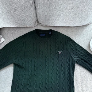 Grön stickad tröja från Gant - Original GANT tröja  Säljer en äkta GANT tröja i mörkgrön färg med klassiskt kabelstickat mönster. Storlek: M Köpt från Zalando  Använd endast ett fåtal gånger, i mycket fint skick.   .