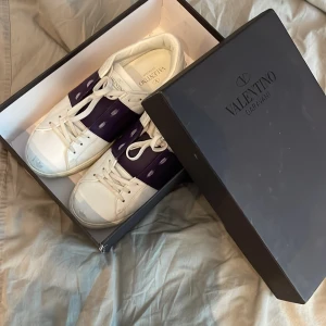 Valentino Garavani sneakers i vitt och lila - Snygga Valentino Garavani sneakers i vitt med lila detaljer. Skorna har en klassisk rund tå och snörning framtill. Perfekta för en stilren look. Skorna kommer med minimala defekter och vill gärna att ni kommer upp med förslag till pris då jag sätter dessa för 2299 och kan gå lägst som 1900 så PRIS GÅR ATT DISKUTERAS. Vid snabba affärer kanske tilll och med lägre 