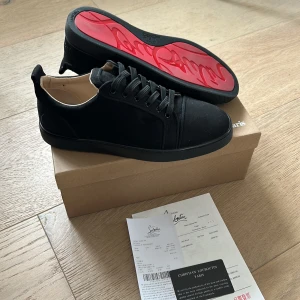 Svarta sneakers från Christian Louboutin - Snygga svarta sneakers från Christian Louboutin med den ikoniska röda sulan. Skorna har en stilren design med snörning och rund tå, perfekt för en trendig look. 