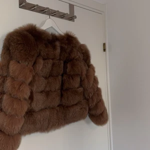 Brun pälsjacka - Säljer en lyxig brun pälsjacka med en mjuk och fluffig textur. Jackan har en elegant design med långa ärmar och en fin glansig insida. Perfekt för att hålla sig varm och stilren under kyliga dagar. Använd en gång. Nypris 4499