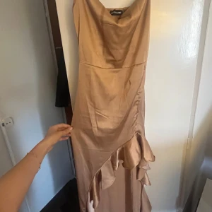 Champagnefärgad Balklänning - Jag säljer min eleganta champagnefärgade klänning från PrettyLittleThing med volangdetaljer. Klänningen har en smickrande passform och är perfekt för speciella tillfällen som bal/bröllop. Materialet ger en lyxig känsla och färgen går att matcha till allt. 