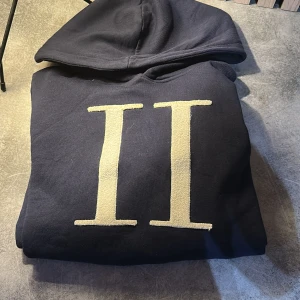 Mörkblå hoodie från Les Deux - Säljer en stilren mörkblå hoodie från Les Deux med en stor vit romersk siffra 'II' på framsidan. Perfekt för en avslappnad stil. Hör av dig vid intresse!