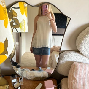 Vit plisserad ärmlös topp - Säljer en stilren vit plisserad topp med halterneck-design. Toppen är ärmlös och har en luftig passform, perfekt för varma dagar. Den är elegant och lätt att matcha med olika outfits. 