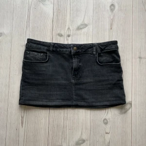 Grå lågmidjad jeanskjol  - Grå/svart lågmidjad jeanskjol från America Today i storlek M. Tvärs över midjan är det 40 cm och den är 28 cm lång. Använd gärna köp nu!