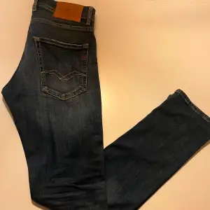 Snygga mörkblå jeans från Replay med klassisk femficksdesign och knappgylf. Jeansen har en stilren look med diskreta sömmar och en läderpatch med logga på baksidan. Perfekta för en avslappnad stil.
