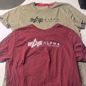 T-shirts från Alpha Industries - Två snygga t-shirts från Alpha Industries i storlek M. En i vinröd och en i olivgrön, båda med det ikoniska Alpha Industries-logotypen tryckt på framsidan. Perfekta för en avslappnad stil.