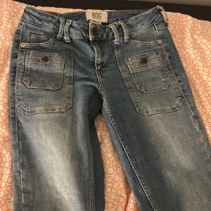 Blå jeansbyxor från BDG - Snygga blå lowaist jeansbyxor från BDG urban outfiters med bootcut-stil. Byxorna har fram- och bakfickor med knappar och en broderad logga på bakfickan. Är i så bra skick! Är i storlek 26W 32L pris kan diskuteras 