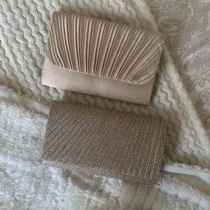 Två eleganta kuvertväskor i guld och beige - Säljer två stiliga kuvertväskor. Den ena är i skimrande guld med glittrig yta, perfekt för att dra blickarna till sig. Den andra är i en elegant beige nyans med veckad design på locket. Båda är perfekta för en kväll ute eller till bal.