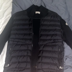 Svart Moncler Cardigan jacka - Snygg svart Moncler cardigan jacka med dragkedja och långa ärmar. Jackan har en stilren design med ribbade detaljer vid ärmslut och nederkant. Perfekt för kyligare dagar. Knappt använd bra skick! Pris kan diskuteras. Står ej för frakten, kan mötas upp i GBG!