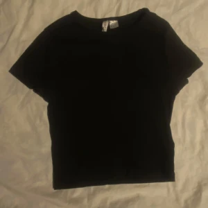 Svart t-shirt från HM - Säljer en basic svart t-shirt från HM. Perfekt basplagg med korta ärmar och rund halsringning. Passar till alla tillfällen och är lätt att matcha med andra kläder. T-shirten är lite kort, man kan se naveln. Kvaliten är bra. Priset kan diskuteras.