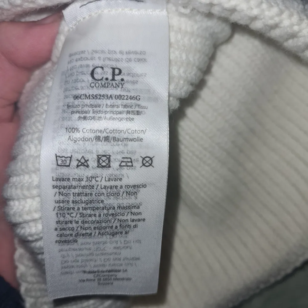 Snygg vit mössa från C.P. Company med unika glasögondetaljer på framsidan. Tillverkad i 100% bomull för en bekväm passform. Perfekt för att ge din outfit en cool touch.. Asusteet.