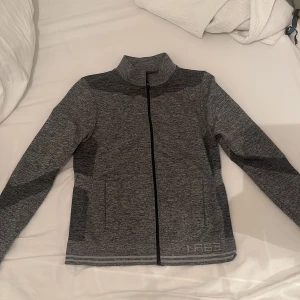 Grå träningjacka med dragkedja - Snygg grå jacka med dragkedja och hög krage. Perfekt för en sportig look och även för träning . Jackan har ett mjuk material 