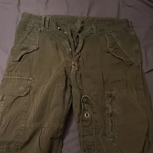 Gröna cargopants med fickor - Säljer ett par gröna cargopants med flera praktiska fickor och knappar. Byxorna har en loose passform och är perfekta för en avslappnad stil. De har en midwaist design och är tillverkade i bomull.