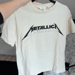 Beige Metallica t-shirt - Säljer en beige t-shirt från H&M med Metallica-tryck i svart. Perfekt för alla rockälskare! T-shirten har en klassisk passform och korta ärmar. Skön och lätt att matcha med jeans eller shorts. Önskar du veta exakta mått? Tveka inte att höra av dig!