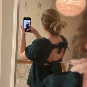 Mörkgrön topp med knyt - Säljer en stilren mörkgrön topp med knyt i ryggen. Toppen har en fyrkantig urringning och puffiga trekvartsärmar. Perfekt för en chic look!