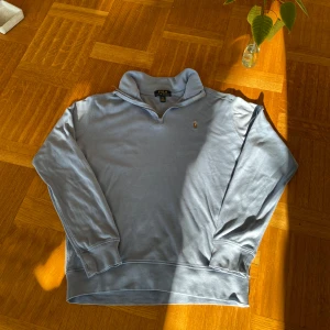 Ljusblå tröja från Polo Ralph Lauren - Säljer en ljusblå tröja från Polo Ralph Lauren med dragkedja vid halsen och det klassiska broderade logotypen på bröstet. Tröjan har långa ärmar och är perfekt för en avslappnad stil. Passar bra till både jeans och chinos.