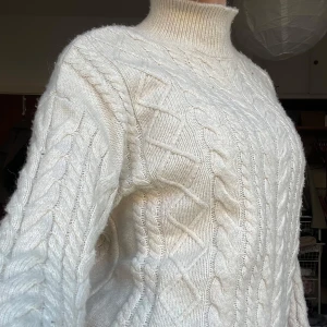 Vit stickad polotröja - Säljer en mysig vit stickad polotröja med kabelstickat mönster. Tröjan har långa ärmar och en hög polokrage som håller dig varm under kyliga dagar. Perfekt för höst och vinter!