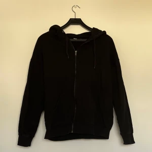 Svart hoodie med dragkedja - Klassisk svart hoodie med dragkedja och huva. Perfekt för en avslappnad stil. Den har långa ärmar och ribbade muddar vid ärmslut och nederkant. Enkelt och stilrent plagg för alla tillfällen.💕