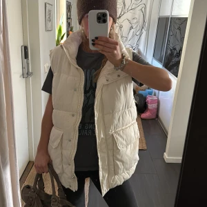 Vit dunväst från H&M - Säljer en stilren vit dunväst från H&M. Västen har en hög krage och stängs med både dragkedja och knappar❣️
