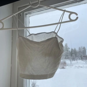 Vit topp/linne - Säljer en stilren vit topp/linne med smala axelband. Perfekt för varma sommardagar eller som ett lager under en kavaj. Enkel och elegant design som passar till det mesta.