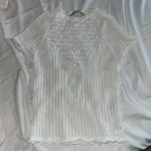 Vit stickad topp från Zara - Säljer en vit stickad topp från Zara med ett fint mönster framtill. Toppen har korta ärmar och en rund halsringning. Perfekt för en stilren look.