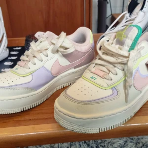 Nike Air Force och Adidas Stan Smith sneakers - Säljer ett par Nike Air Force sneakers storlek 39 i pastellfärger med snörning och ett par klassiska vita Adidas Stan Smith i storlek 40.2/3med gröna detaljer. Nike-skorna har en mix av rosa, lila och grönt medan Adidas-skorna är helvita med gröna hälflikar. Basketkängor med Nike-märke i guld, storlek 42.5, sjukt snygga! Pris för Airforce 400 kr, Stan Smith 300 kr, Basketkängor 250 kr. Eventuell frakt tillkommer!