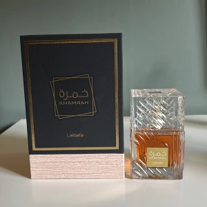 Khamrah Parfym från Lattafa - Elegant parfym från Lattafa med namnet Khamrah. Flaskan är fyrkantig och genomskinlig med ett vackert mönster och en gyllene etikett. Doften är en Eau de Parfum och kommer i en stilren förpackning med svart och guld design. Perfekt för den som söker en sofistikerad och unik doft. 96/100ml kvar 