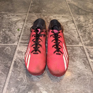 Adidas speedportal 0.3 - Säljer ett par röda fotbollsskor från Adidas med svarta och vita detaljer. Skorna har snörning och en strömlinjeformad design som passar perfekt för snabba rörelser på planen. De har en låg profil och är designade för att ge bra grepp och kontroll.