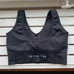 Svart topp från NVGTN - Säljer en stilren svart linnetopp från NVGTN. Toppen har en enkel design med breda axelband och en ribbad nederkant. Perfekt för träning eller en avslappnad dag.