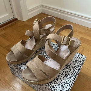 Beige kilklack sandaler - Snygga beige sandaler med kilklack och justerbart spänne. De har en flätad sula som ger en somrig känsla. Perfekta för varma dagar.