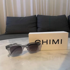 Grå Chimi 04 - Snygga grå solglasögon från Chimi med en stilren och modern design. Bågarna är genomskinliga och fyrkantiga, vilket ger en cool look. Perfekta för soliga dagar och att komplettera din outfit med en touch av stil.