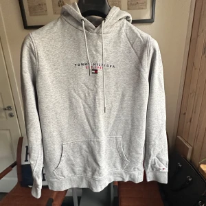 Tommy Hilfiger Hoodie Grå - Säljer en stilren grå hoodie från Tommy Hilfiger med klassisk logga på bröstet. Storlek M. Perfekt för en avslappnad stil.