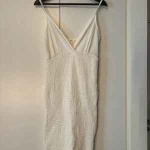 Vit klänning från Object - Säljer en stilren vit klänning från Object med v-ringad design och smala axelband. Klänningen har en texturerad yta som ger en unik look. Perfekt för varma dagar eller sommarens fester. 🌞
