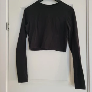 Svart croppad långärmad topp - Säljer en stilren svart croppad topp med långa ärmar. Perfekt för en trendig look. Passar bra till både jeans och kjol.