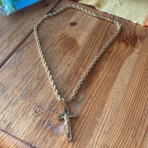18k guld kedja med kors guld planterat 6mm - Snyggt halsband i guldfärg med tvinnad kedja och ett detaljerat korshänge med Jesusmotiv och texten INRI. Korset har svarta detaljer som ger extra kontrast. Perfekt statement-piece för dig som gillar klassiska smycken med en twist.
