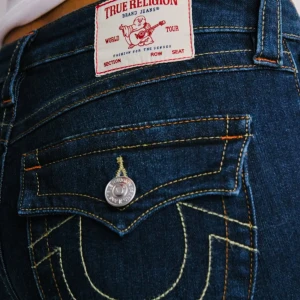 True Religion mörkblå bootcut jeans - Mörkblå jeans från True Religion med ikoniska kontrastsömmar och snygga fickdetaljer med lock och silverknapp. Modellen har bootcut-snitt och normal passform. Klassisk femficksdesign och högkvalitativt denimtyg.Aldrig andvänt pga storlek. ❤️❤️. Helt nya. 
