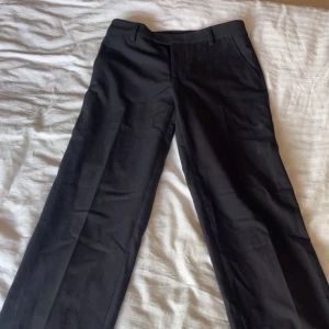 Svarta kostymbyxor - Snygga svarta kostymbyxor med raka ben. Klassisk design med sidfickor fram och knäppning bak på fickorna. Perfekta för en clean och stilren look.
