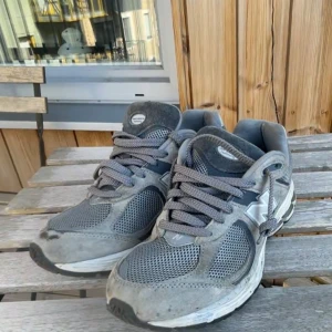 Grå New Balance 2002R sneakers - Snygga New Balance 2002R sneakers i olika grå nyanser med mesh och mockadetaljer. Skorna har klassisk snörning, rund tå och platt sula. Perfekta för dig som gillar streetwear och vill ha en bekväm och stilren sneaker till vardags.