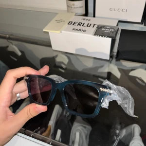 Blåa solglasögon från Berluti - Snygga solglasögon från Berluti. Bågarna är i en djup blå färg och har diskreta silvriga detaljer vid gångjärnen. Kommer med originaletui och putsduk. Perfekt accessoar för att lyfta din stil.💙🦕