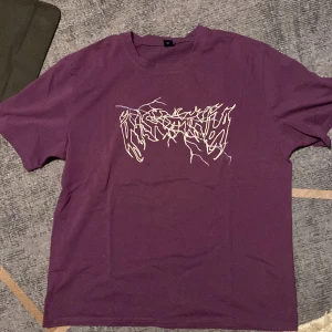 Lila t-shirt med grafiskt tryck från Romwe - Säljer en lila t-shirt från Romwe i storlek M. T-shirten har ett vitt grafiskt tryck framtill med coolt, abstrakt mönster. Klassisk passform med rund hals och korta ärmar. Perfekt för dig som vill sticka ut med en unik vibe.