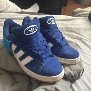 Blå campus 00s adidas sneakers - Snygga blå adidas sneakers med . Ovandel i mocka, vit sula och blå snörning, men finns tillhörande vita snören. Låda tillkommer och lappen finns kvar. Skorna är endast testade inomhus och säljs för dom är för små. Pris går att diskutera.