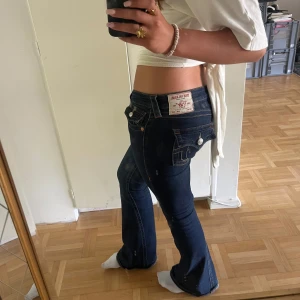 True Religion mörkblå bootcut jeans - OBS! Spegeln är smutsig. Säljer ett par mörkblå jeans från True Religion som knappt är använda pågrund av att det är förstora för mig. De har inga hål eller slitningar någonstans. Jeansen har låg midja och bootcut passform, tillverkade i stretchig denim för en snygg siluett. 