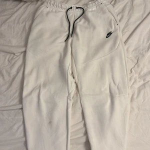 Vita mjukisbyxor från Nike - Snygga vita mjukisbyxor från Nike med svart logga på låret och svarta snören i midjan. Byxorna har elastisk midja och är perfekta för en chill och sportig look. Mjukt material som känns skönt mot huden.