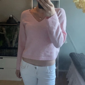 Ljusrosa stickad tröja från 157 - Supermjuk ljusrosa stickad tröja från 157 med v-ringad hals och lång ärm. Tröjan har en croppad passform och ribbade muddar vid ärmslut och nederkant. Perfekt för dig som gillar en söt och enkel stil.